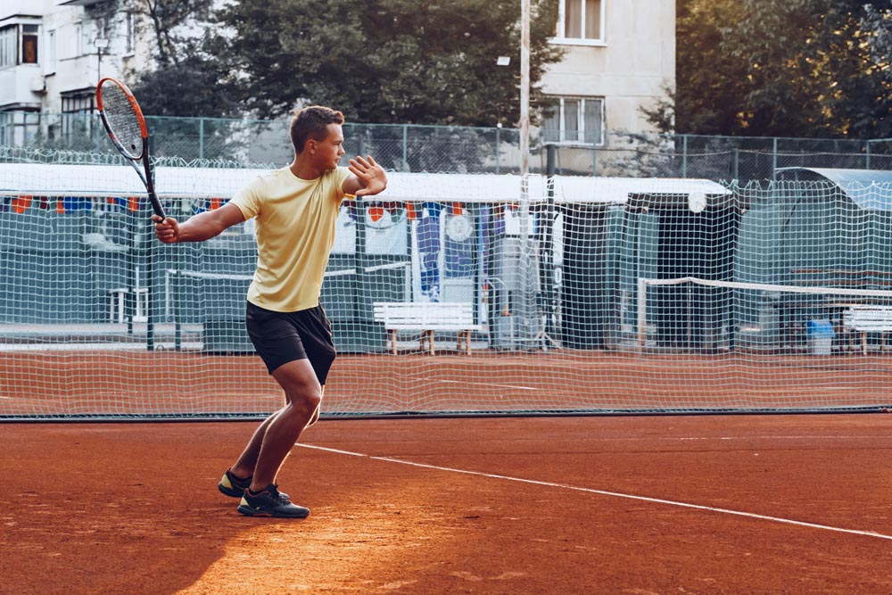 Young handsome man playing tennis on the clay tennis court